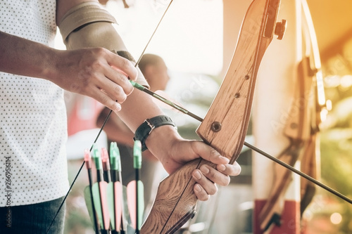 Tourists try to use a bow and arrow and shoot at a target in the amusement park.