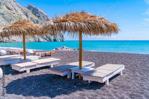 Empty deck chairs and umbrellas on the black sand beach in Perissa, Santorini, Greece