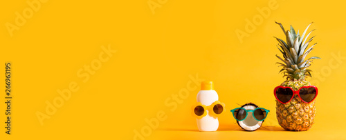 Pineapple and coconut wearing sunglasses with sunblock on a solid background