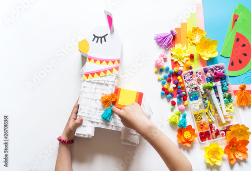 Diy cinco de mayo Mexican Pinata llama made cardboard and crepe paper your own hands on a white background.