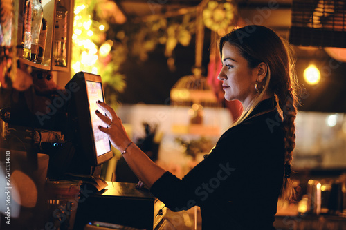 Concepto pequeño negocio o emprendimiento personal: una joven camarera en la máquina registradora de un bar o restaurante