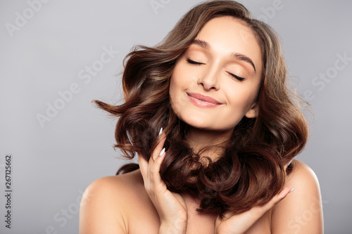 Brunette girl with healthy curly hair and natural make up . Beautiful model woman with wavy hairstyle .Care and beauty