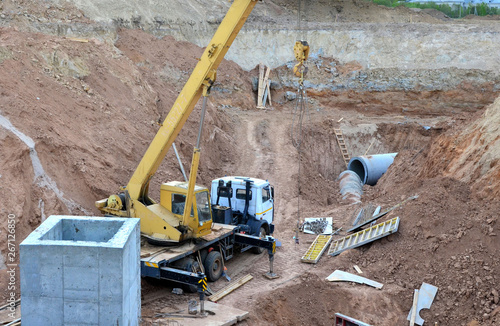 Crane operation in the pit, laying or replacement of underground storm sewer pipes at the construction site. Installation of water main, sanitary sewer and storm drain systems. Utility Infrastructure