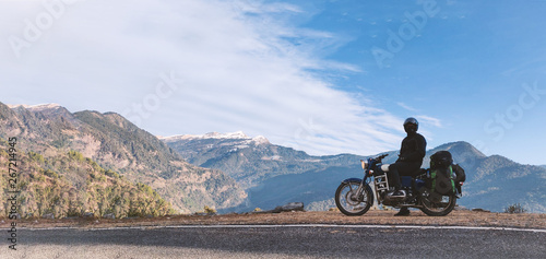 A young unidentifiable man sitting on his motorbike with view of Himalayan mountains.