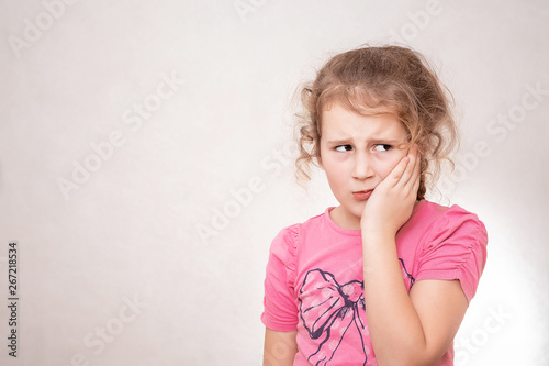 Cute little girl with Dental problem, having severe pain and almost crying. Standing isolated over gray background