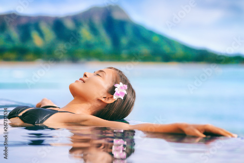 Hawaii vacation luxury resort travel Asian tourist girl relaxing in hotel infinity pool by Waikiki beach in Honolulu, Oahu. USA travel.