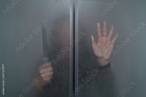 girl with a knife in his hand behind the glass door of the shower in the bathroom