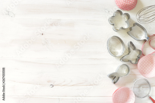 Set of cookies cutters and paper tins on a white wooden background