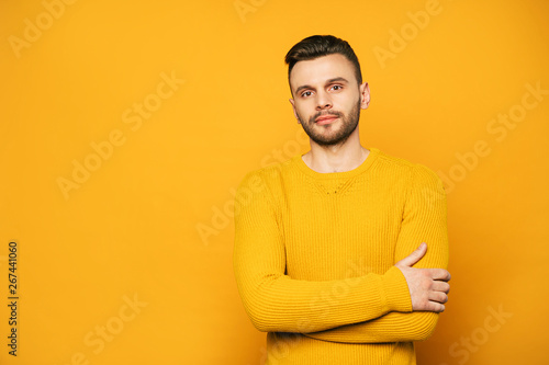 Confident handsome man in yellow is posing over orange background and looks on camera