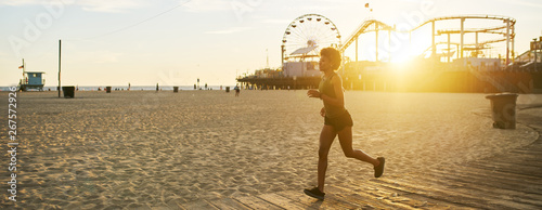 athletic african american woman jogging on boardwalk at sunset