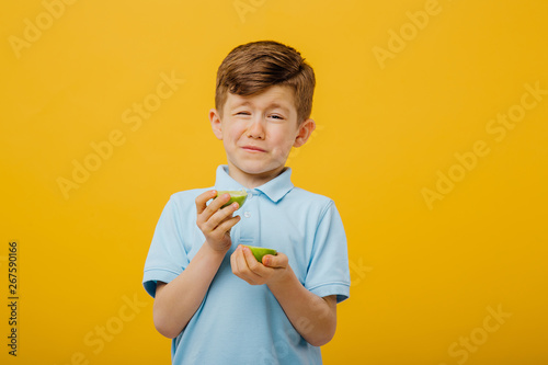 beautiful boy taste a fresh lime taste sour grimace, facial emotions negative, in blue T-shirt, isolated yellow background, copy space