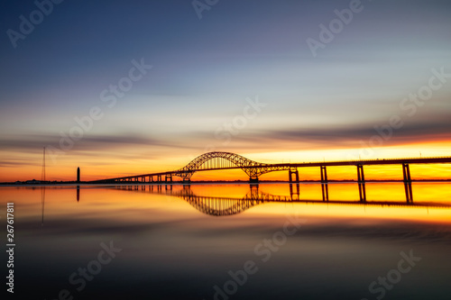 Long silhouetted bridge with an arch crossing a crystal clear calm body of water at sunset. Perfect reflections in the water - Long Island New York. 