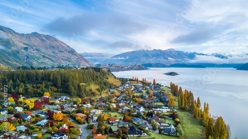Small town surrounded by yellow autumn trees on a shore of pristine lake with mountains on the background. Wanaka, Otago, South Island, New Zealand