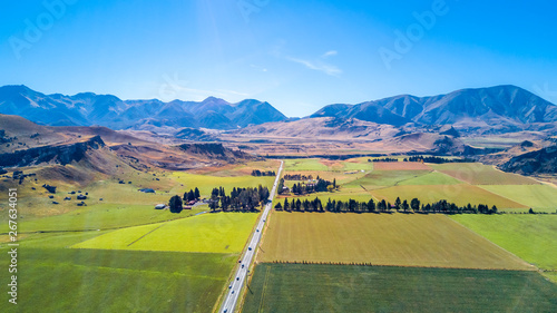 Road running through farmland with mountains on the background. West Coast, South Island, New Zealand