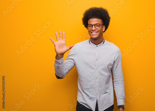 Young african american man over an orange wall showing number five