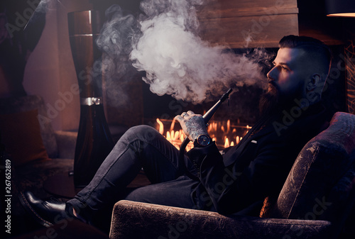 Elegant smart man is relaxing and smoking hookah after long hard day.