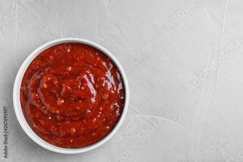 Bowl of hot chili sauce on light background, top view. Space for text