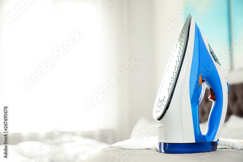 Modern electric iron on board indoors, space for text. Household appliance