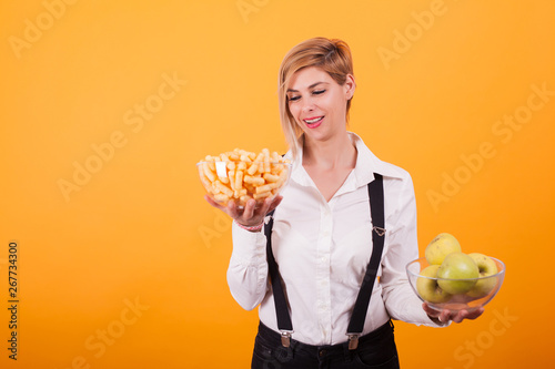 Pretty blonde woman with short hair looking at her bowl of green apples over yellow background.