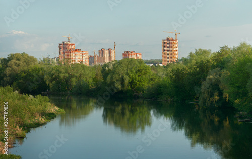 Construction of high-rise buildings on the background of blue sky. Multi-storey buildings under construction in the park near the river