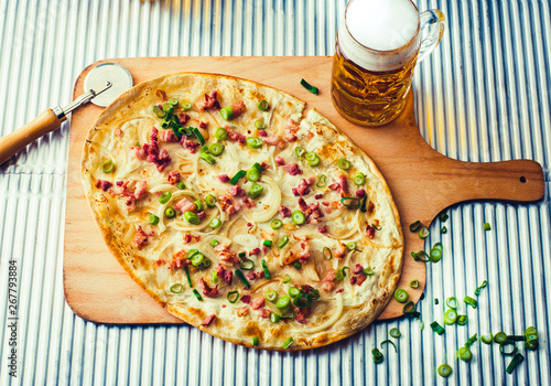 Tarte flambe or Flammkuchen with bacon and onions on wooden cutting board with a glass of beer