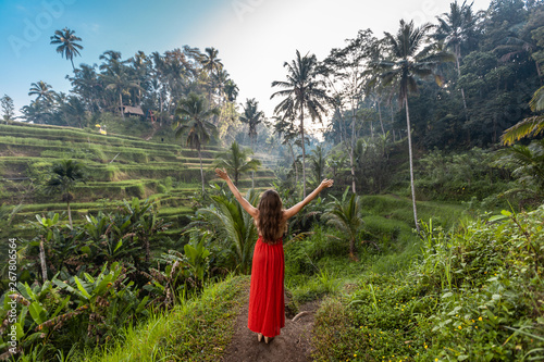 Woman with open arms in red dress on rice fields Bali in Tegallalang. Rustic Ubud village landscape outside. Fashion style