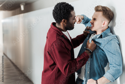 two multiethnic students fighting in corridor in college