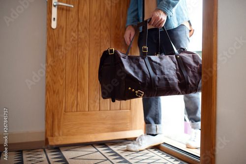 Midsection of young man with bag entering front door when coming back home.