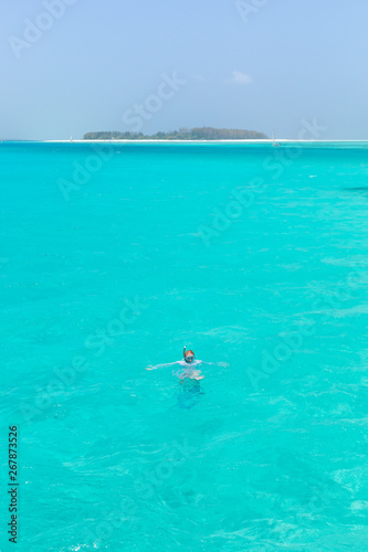Woman snorkeling in clear shallow sea of tropical lagoon with turquoise blue water and coral reef, near exotic island. Mnemba island, Zanzibar, Tanzania.