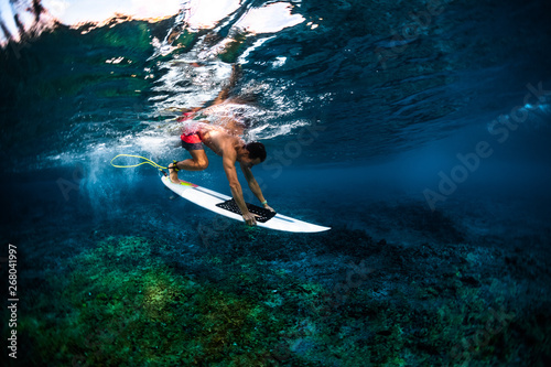 Surfer dives under the wave with his surfboard over the sharp reef with uneven surface