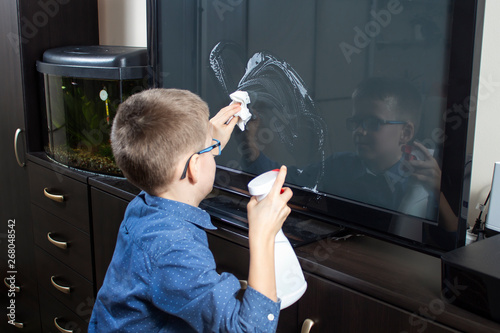 Wycieranie ekranu telewizora z kurzu przez chłopca w wieku szkolnym. 