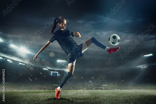 Młoda kobieta piłkarz lub piłkarz z długimi włosami w odzieży sportowej i buty kopanie piłki do bramki w skoku na stadionie. Pojęcie zdrowego stylu życia, profesjonalnego sportu, hobby, ruchu, ruchu