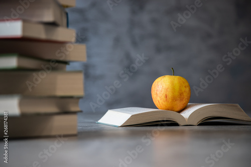 Jabłko leżące na otwartej ksiązce obok stosu lektur na tle betonu