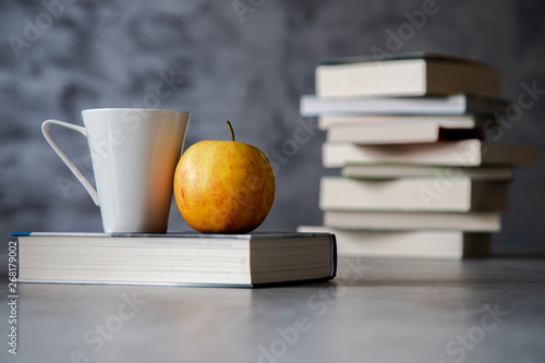 Kubek i jabłko na książce, a w tle stos książek