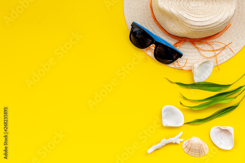 Planning vacation to the seaside with straw hat, sun glasses, shells on yellow background top view space for text