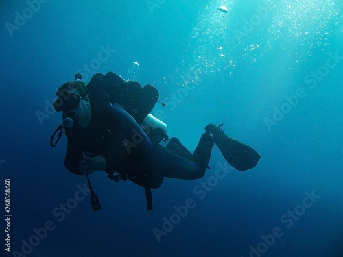 Scuba diver with full equipment is underwater. Sunlight and bubbles. 