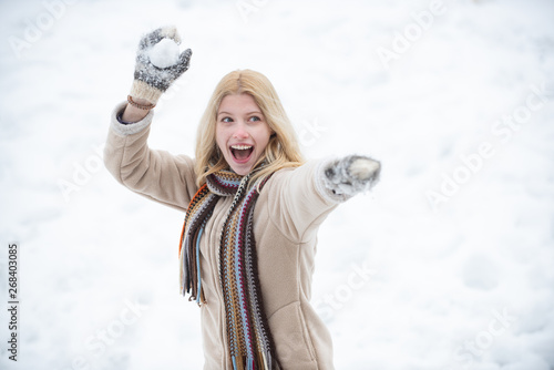Snowball fight. Woman holding the snowball in hands. Models having fun in winter park. Happy woman winter portrait. Winter emotion.