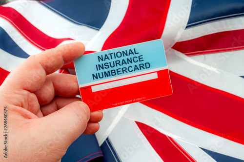 Social security system, access to safety net programs in Great Britain concept theme with a blank National Insurance Number card or NINO held in one hand with the UK flag in the background