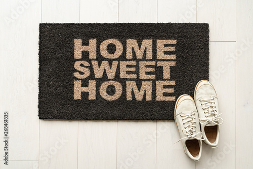 Home sweet home door mat at house entrance with women's sneakers of woman that has just arrived moved in. New condo.