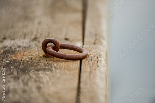 Wooden deck of a pier with a worn, rusty metal ring for mooring a boat.