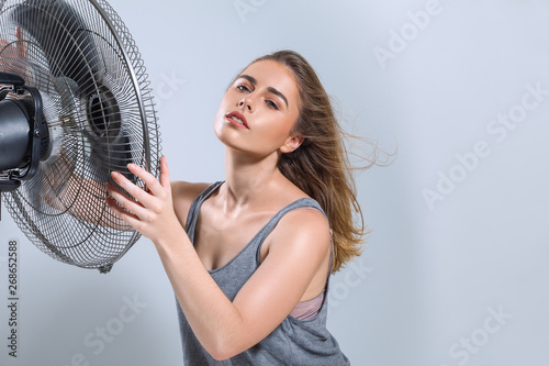 Young woman enjoying cool wind from electric fan