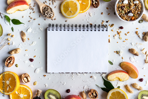 Healthy food nutrition concept, fresh summer fruits nuts granola seeds and empty blank notebook on white background, organic super food on table, detox diet for health care, top view, copy space