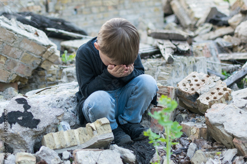 Little boy near the destroyed house. Child trouble, loneliness concept.