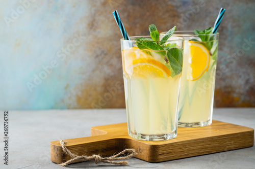 Two glass with lemonade or mojito cocktail with lemon and mint, cold refreshing drink or beverage with ice on rustic blue background. Copy space