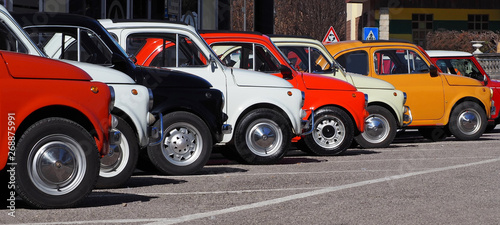  A row of colorful vintage Fiat 500 s in a roadside parking lot on a sunny day.