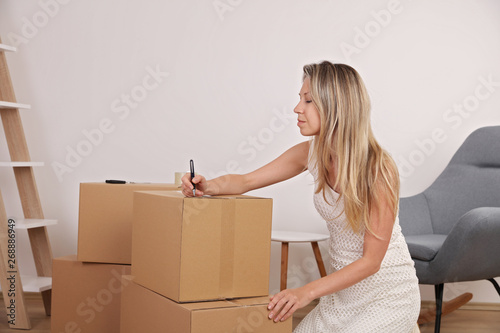 Moving in and out. Woman packing and labeling moving box at home