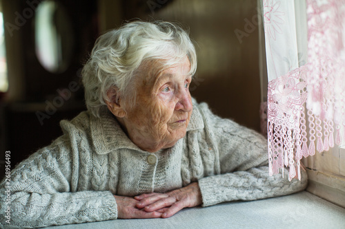 An elderly old woman looks sadly out the window. Care for lonely pensioners.