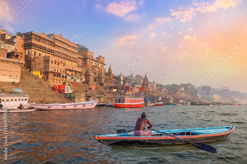 Historic Varanasi city architecture at sunset with view of a boatman rowing on river Ganges