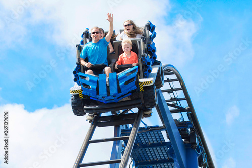 Young family having fun riding a rollercoaster at a theme park. Screaming, laughing and enjoying a fun summer vacation together.