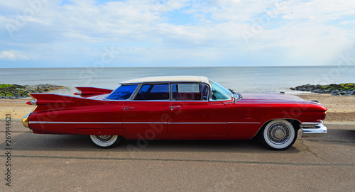 Classic Red 1950's 4 door Cadillac motor car parked on seafront promenade.